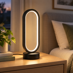 Oval LED ring table lamp glowing warm white on a bedroom nightstand